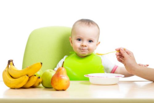 Ребенка за столом кормят из ложечки